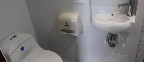 A small bathroom with a toilet, a hand sanitizer dispenser, and a sink.