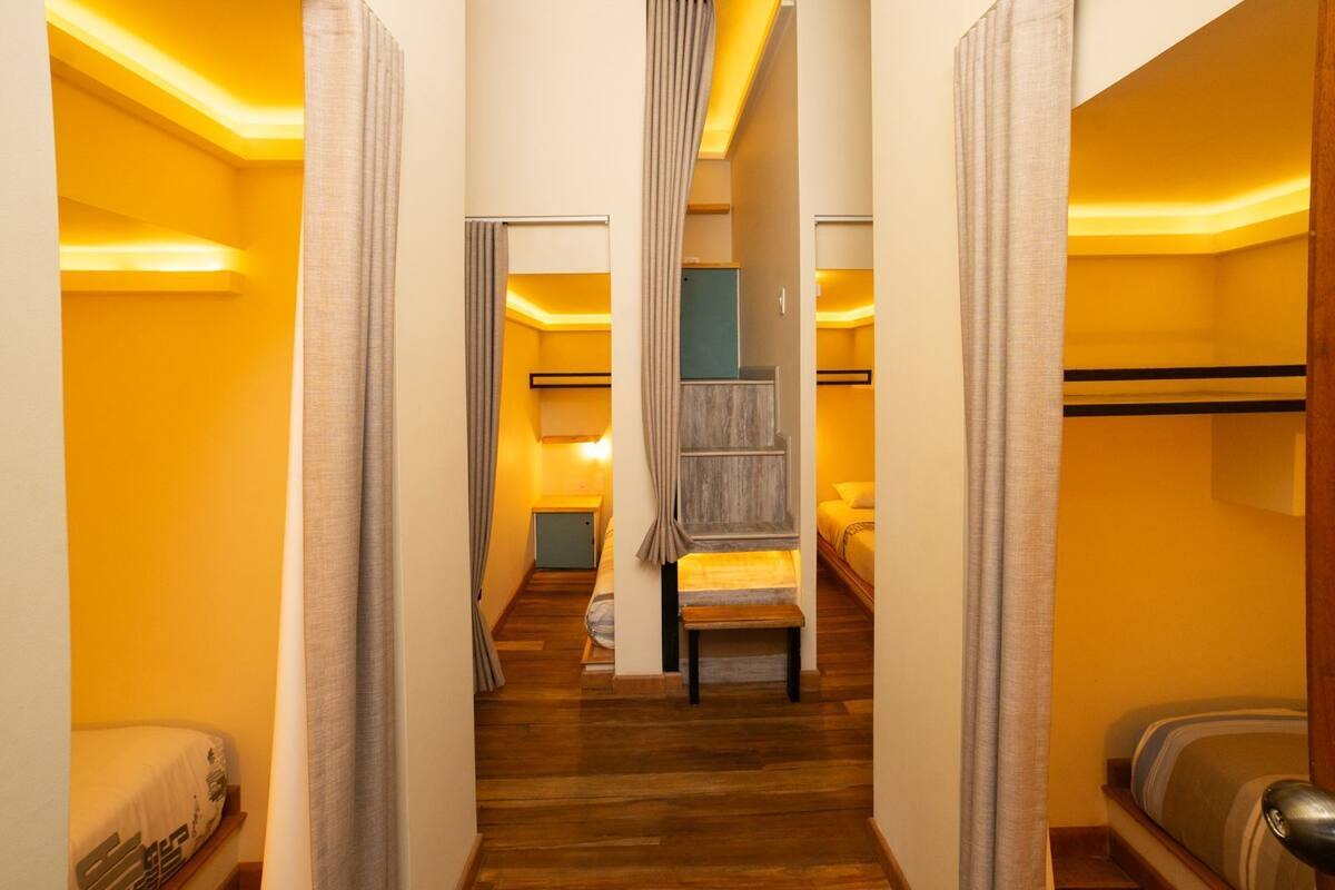 Un passadís estret amb terres de fusta que condueix a una habitació amb un llit i un petit escriptori.