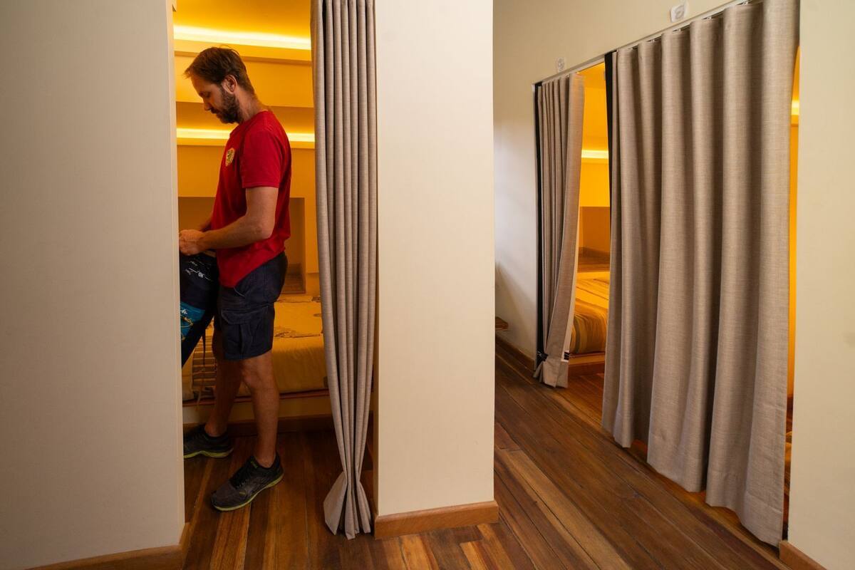 Una habitació d'hotel amb terra de fusta, un llit amb edredó groc i una persona dempeus a prop de la porta.