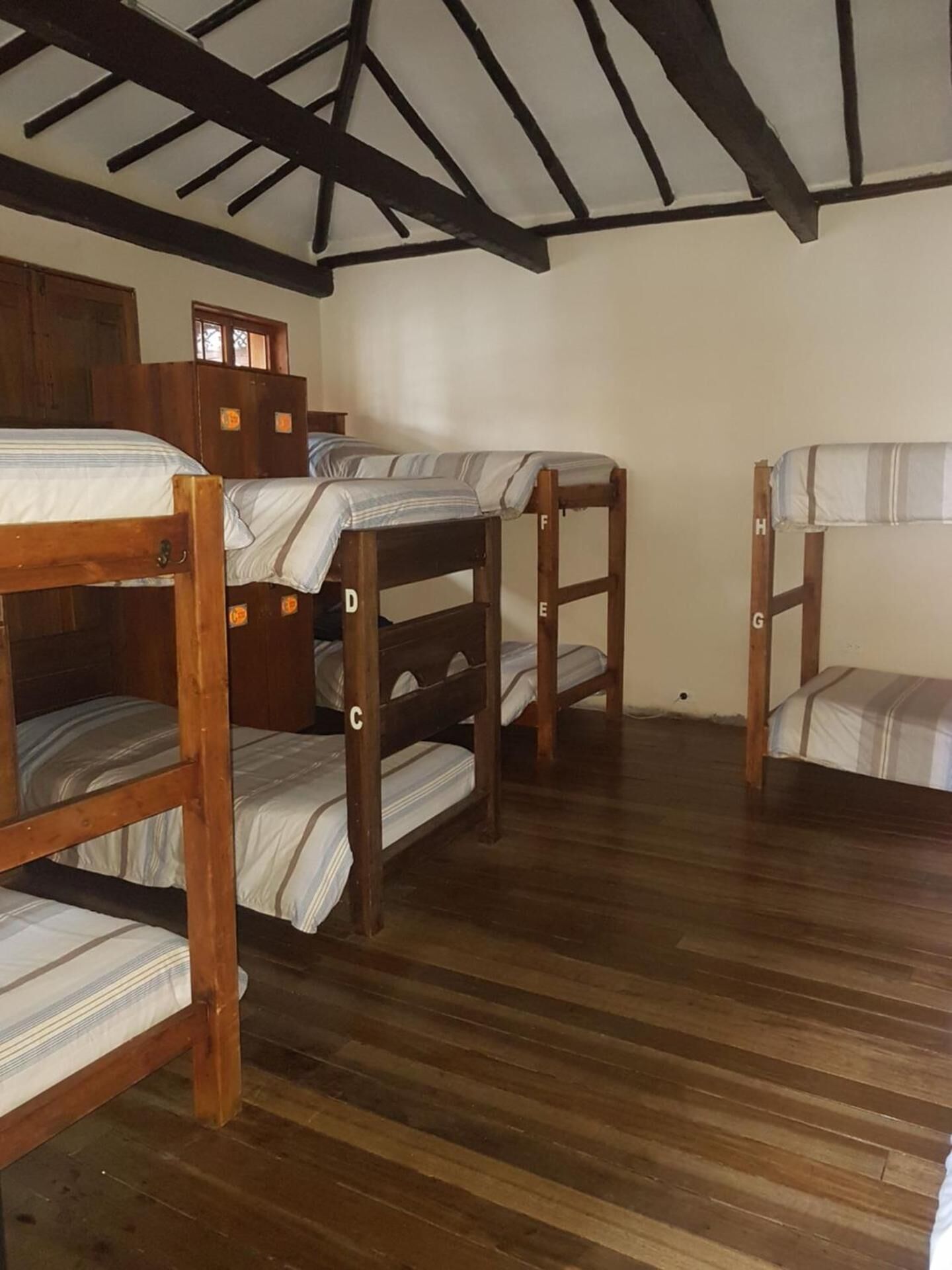 A room with four wooden bunk beds, a wooden wardrobe, and a sloped ceiling with exposed beams.