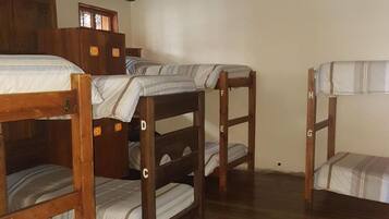 A room with four wooden bunk beds, a wooden wardrobe, and a sloped ceiling with exposed beams.