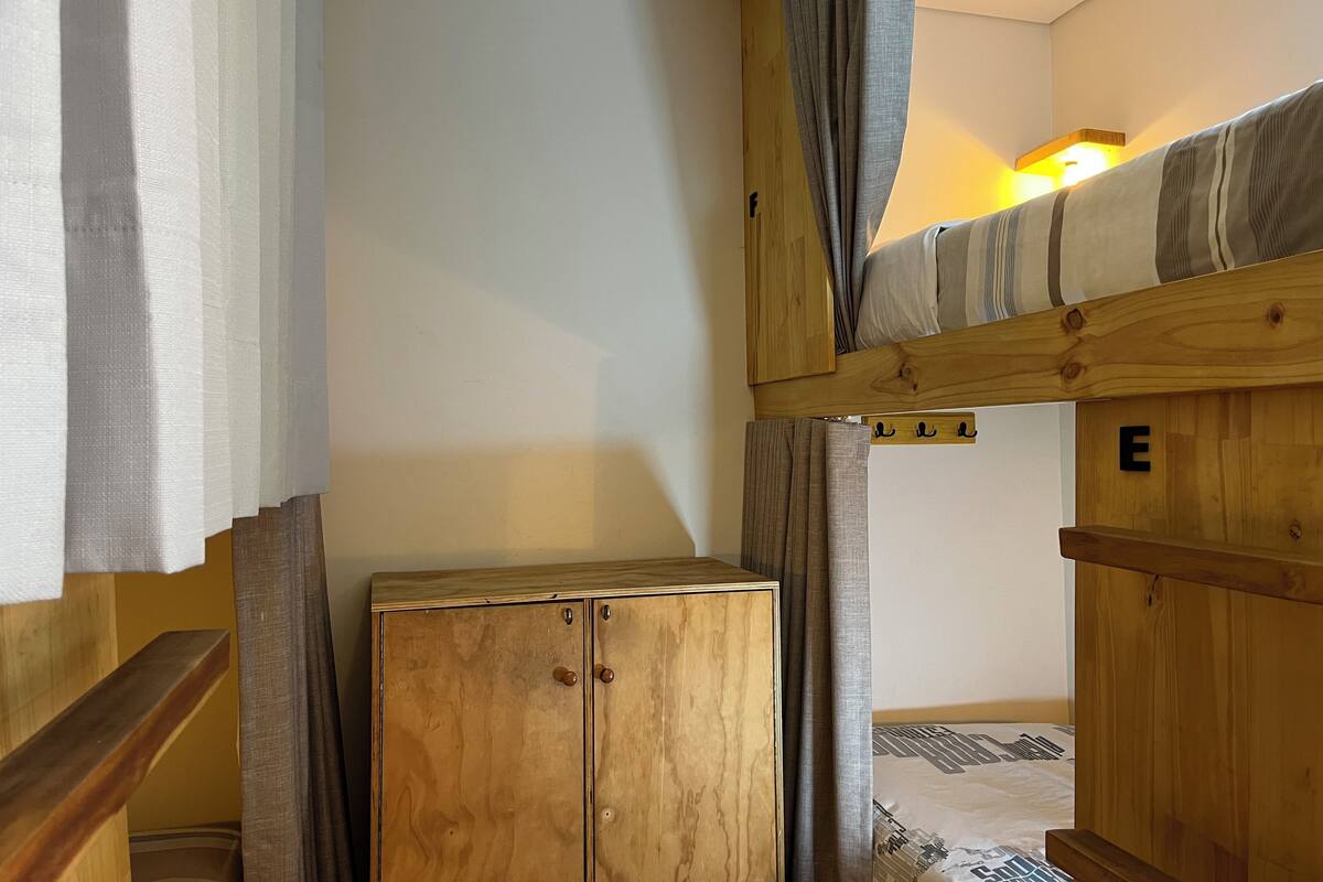 Un llit superposat amb capçalera i peanya de fusta, un armari i una làmpada fixada a la paret.
