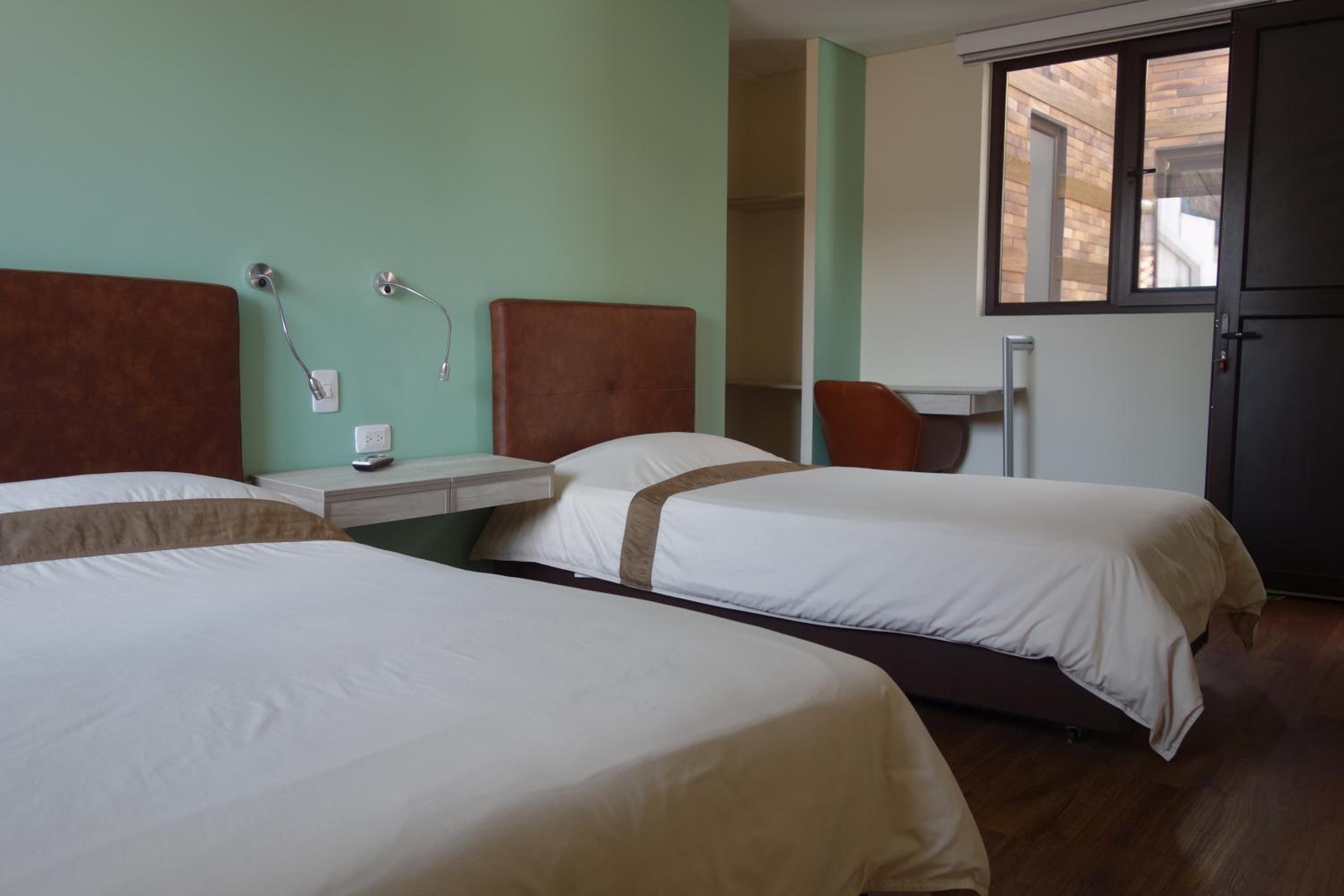 A hotel room with two beds, a small table, a chair, and a window.