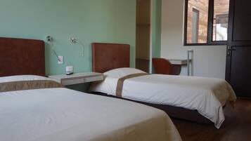 A hotel room with two beds, a small table, a chair, and a window.