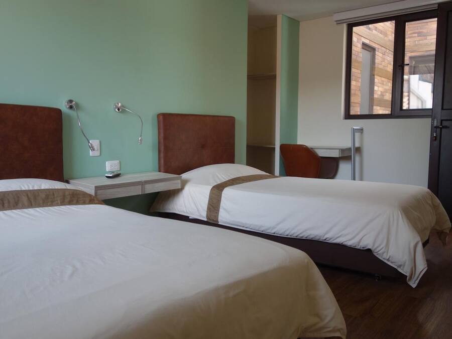 A hotel room with two beds, a small table, a chair, and a window.