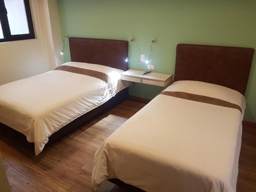 Two single beds with brown headboards, a bedside table with a remote control, and a wall socket.