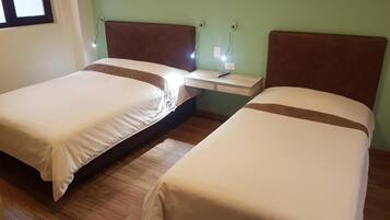 Two single beds with brown headboards, a bedside table with a remote control, and a wall socket.