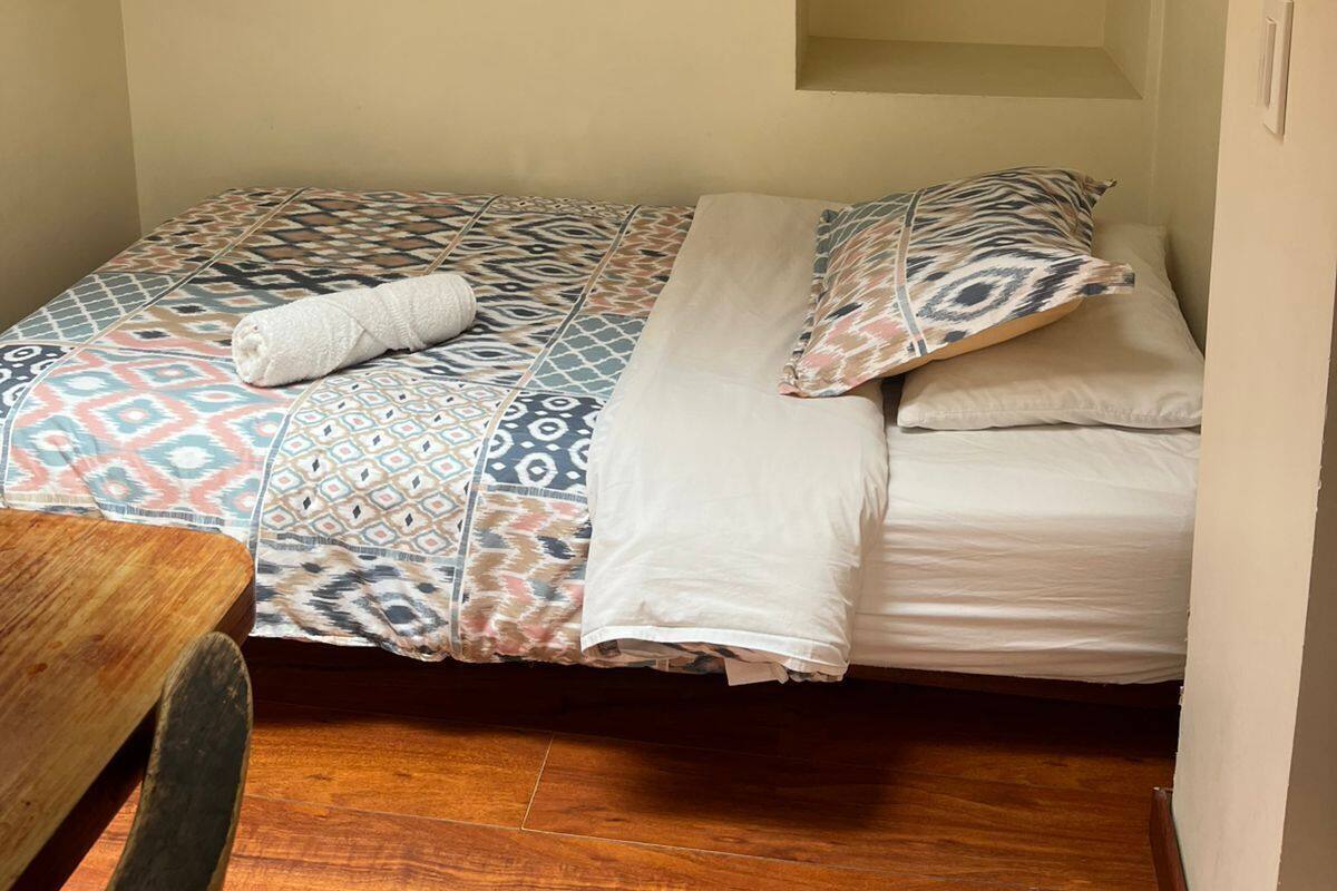 Una habitació petita i acollidora amb un llit, una taula de fusta i un sostre inclinat amb bigues al descobert.