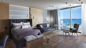 A modern bedroom with a large bed, a sofa, a coffee table, and a chair. There is a large window with a view of the ocean. - Seafront Apt Studio with Seaview, infinity pool, beachfront (Limenas Chersonisou)