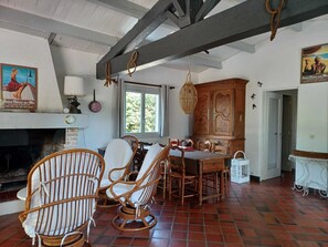 A room with a fireplace, wicker chairs, a dining table, and a large wooden cabinet. - Villa with a large, tree-lined garden near the beach (Saint-Palais-sur-Mer)