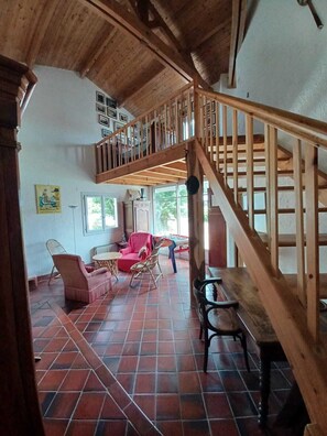 Un vaste espace de vie agrémenté d’un escalier en bois, d’un revêtement de sol carrelé et de différents types de sièges, notamment un canapé et des fauteuils.