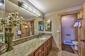 Un baño con encimera de granito, un lavabo, un espejo grande y una puerta de madera.
