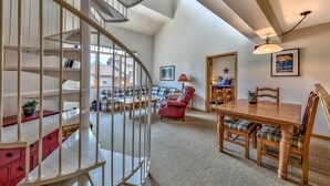 A spacious living area with a spiral staircase, a dining table with chairs, a red armchair, and a sofa set. - Luxury 2br + Loft, Lodge At Kirkwood Unbeatable Location 2 Bedroom Condo by RedAwning (Kirkwood)