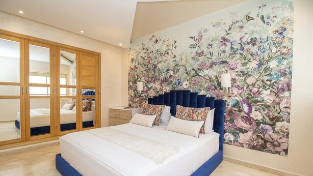 A bedroom with a large bed, a floral mural on the wall, and a sliding door closet. - Studio de Luxe à Casablanca Aireport (Nouaceur)