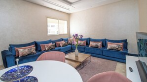A living room with a blue sectional sofa, a coffee table, and a vase with flowers. - Studio de Luxe à Casablanca Aireport (Nouaceur)
