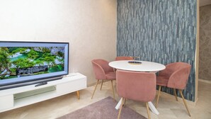 A modern living room with a flat-screen TV, a white entertainment unit, a round white table, and pink chairs. - Studio de Luxe à Casablanca Aireport (Nouaceur)
