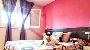 Een slaapkamer met een bed, gordijnen, een nachtkastje en een muur met een raam.