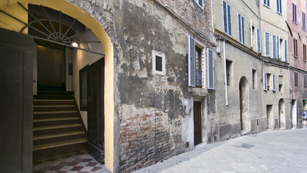 A narrow street with a building featuring a staircase leading to an entrance. - SAN DOMENICO LUXURY APARTMENT (Siena)
