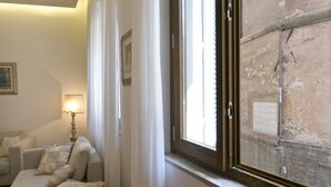 A room with a sofa, a lamp, and a window with a view of an exterior wall. - SAN DOMENICO LUXURY APARTMENT (Siena)