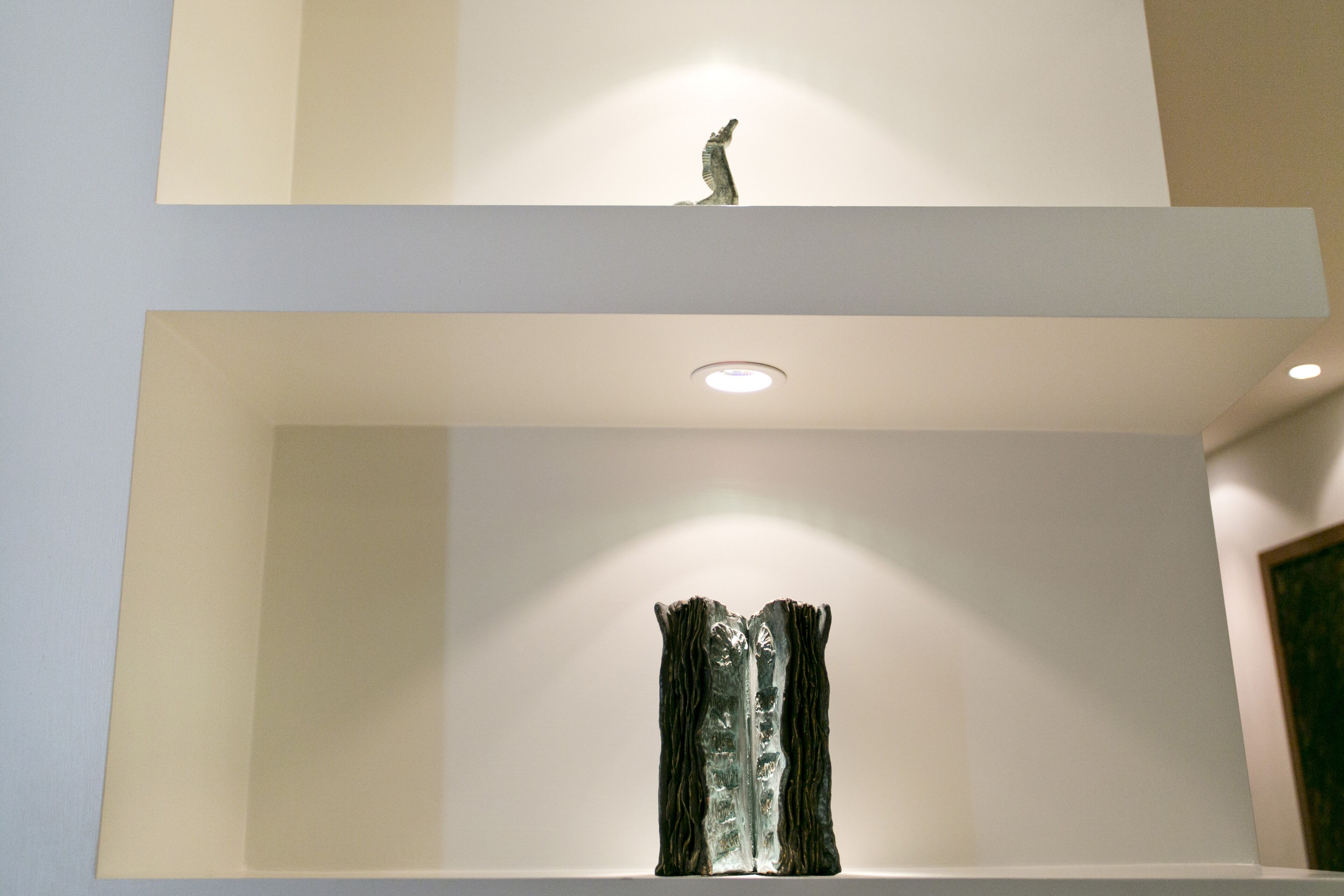 A modern interior with a minimalist design, featuring a sculpture on the upper shelf and a textured piece on the lower shelf.