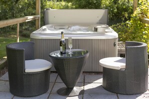 Un bain à remous avec une terrasse en bois, deux fauteuils en osier et une table sur laquelle se trouvent une bouteille et un verre.