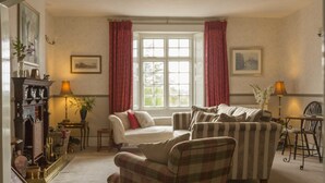 A cozy living room with a fireplace, striped armchairs, a sofa, and a dining table. - The Pines at Eastleigh - 3 Cottages (Bideford)