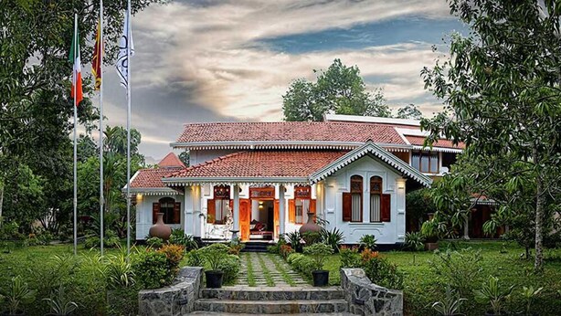 A traditional building with a tiled roof, a central entrance, and a well-maintained garden with stone steps leading to the entrance. - Olcote in Ceylon (Piliyandala)