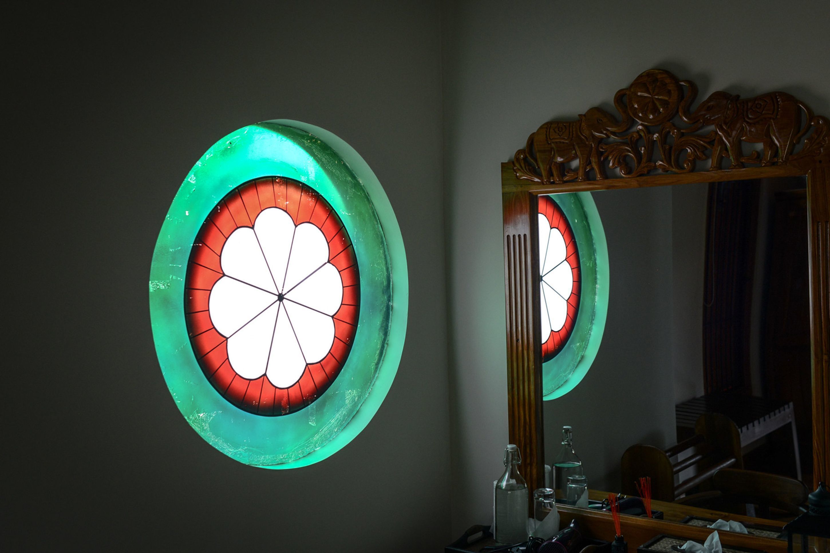 A bathroom with a large mirror, a round stained glass window, and a wooden vanity.