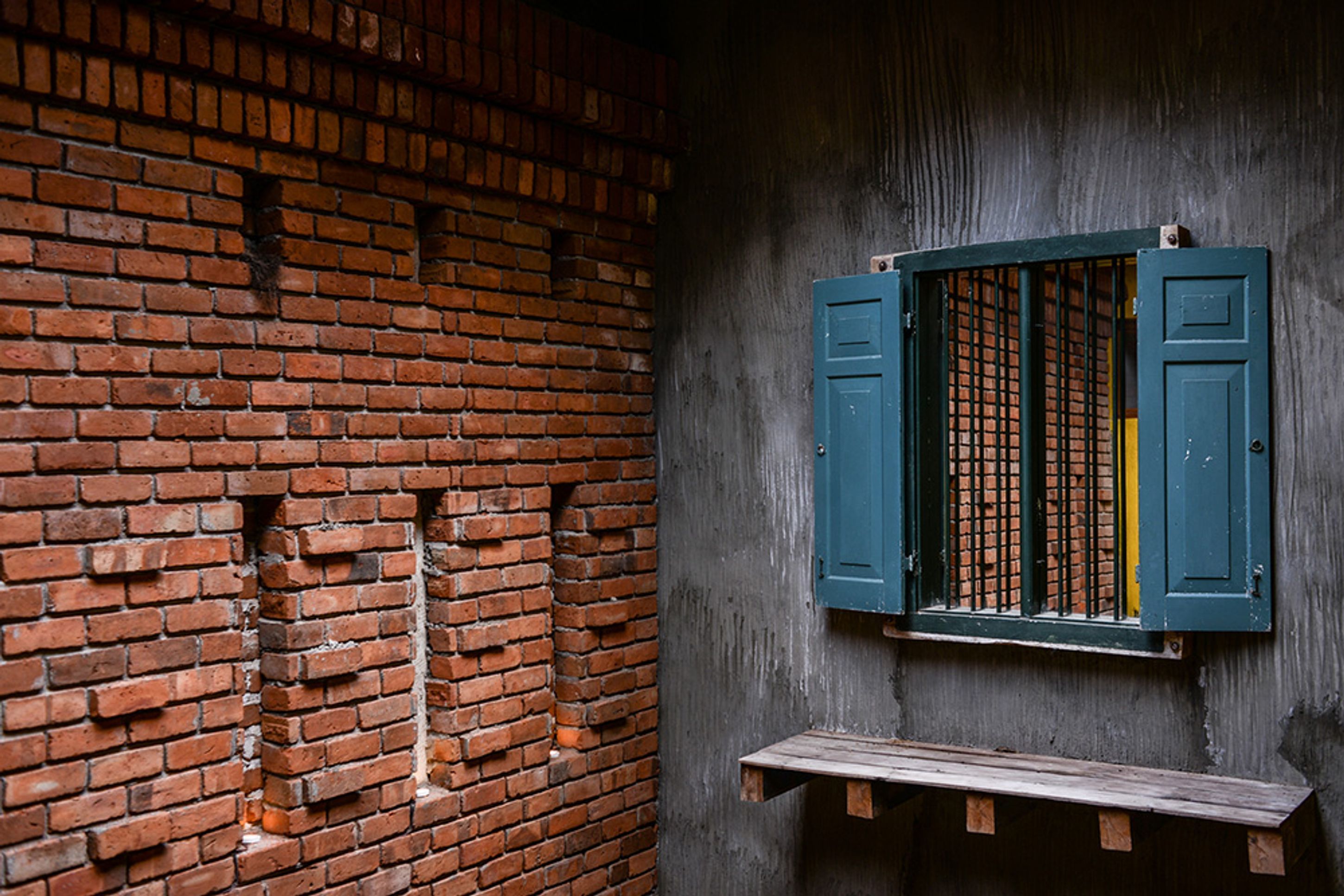A brick wall with a window featuring green shutters.