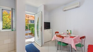 Une pièce de taille modeste, avec une table à manger pour deux personnes, un téléviseur posé sur un meuble et une fenêtre donnant sur un paysage verdoyant.