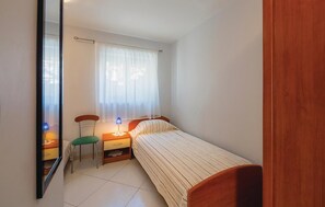 Quarto pequeno e bem organizado com uma cama de solteiro, uma cadeira, mesa de cabeceira e espelho.