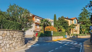 Une rue bordée de murs en pierre, une voiture rouge et des immeubles dotés de balcons et de fenêtres.