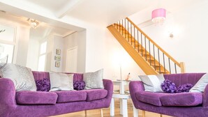 A modern living room with two purple sofas, a wooden staircase, and a chandelier. - SunlightProperties LEGEND: 2 Bedroom Rental, near Beach with balcony & AC (Nice)