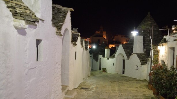 A narrow, stone-paved alleyway flanked by white buildings with arched doorways and small windows. - Trulli Casa Alberobello (Alberobello)