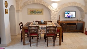 A dining area with a table and chairs, a television, and stone arches. - Trulli Casa Alberobello (Alberobello)