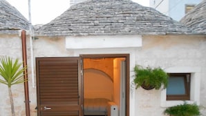 A small stone building with a wooden door, a red mat at the entrance, and potted plants. - Trulli Casa Alberobello (Alberobello)