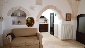 A living room with a beige sofa, a painting, and a kitchen visible through an archway. - Trulli Casa Alberobello (Alberobello)