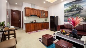 A modern kitchen with wooden cabinets and a black refrigerator, a dining area with a table and chairs, and a living room with a sofa and a painting on the wall. - Aparthanoi (Hanoi)