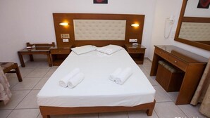 A neatly made bed with white linens and rolled towels, a wooden nightstand with a lamp, a wooden dresser with a mirror, and a single red rose painting on the wall. - Sunrise Apartments Hersonissos (Hersonissos)
