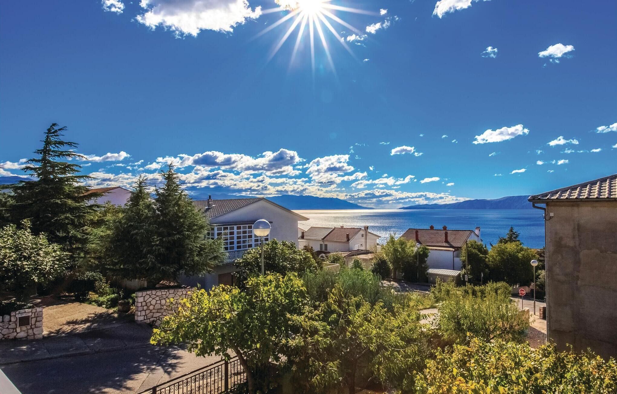 Una zona residenziale lungo la costa, con case, alberi e una vista libera sul mare e sulle montagne sullo sfondo.