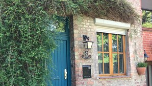 A rustic building with a blue door, a brick wall, a window with a wooden frame, and a black bench outside.