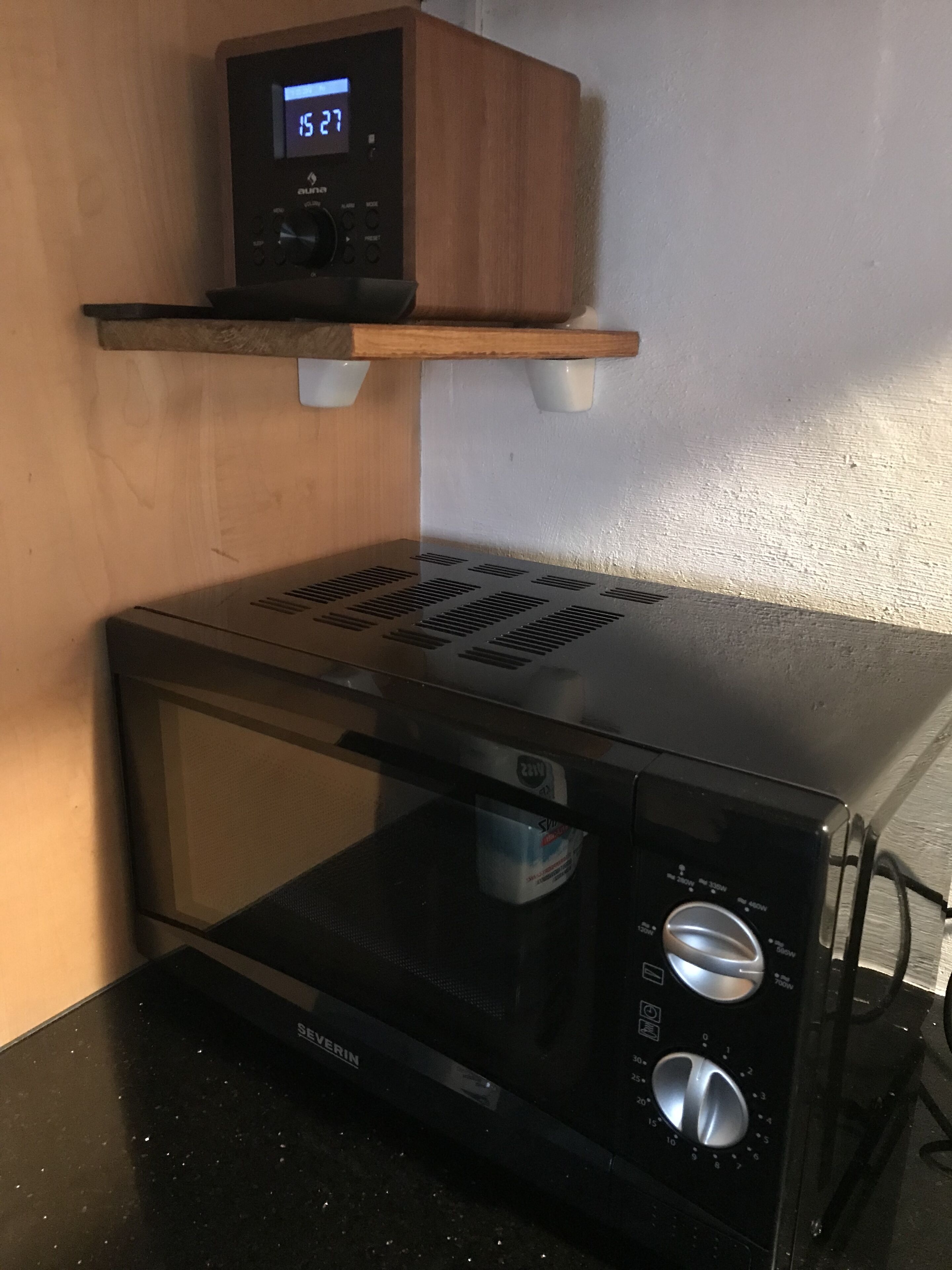 Un horno microondas compacto con pantalla digital y perillas de control, sobre una encimera negra.