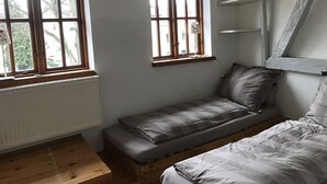 A room with two windows, a radiator, a wooden bench, and a bed.