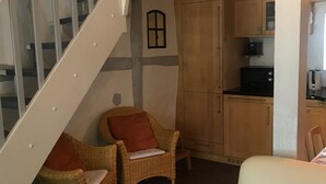 A living area with a staircase, wicker chairs, a sofa, and a kitchen with wooden cabinets and a microwave.