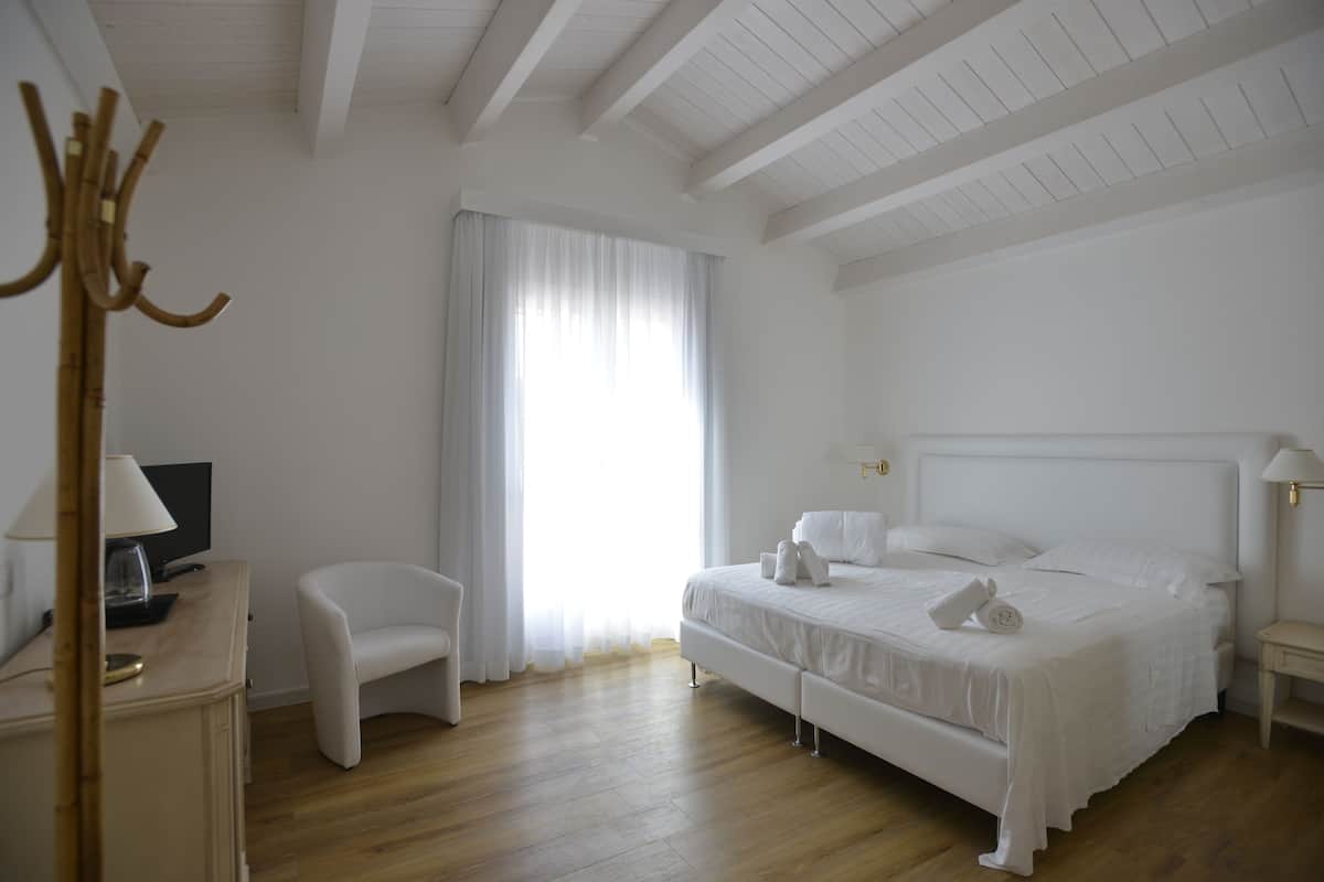 A hotel room with a bed, a chair, a desk with a lamp, and a television.