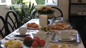 A breakfast table with plates of food, a teapot, and a window with a view of greenery.