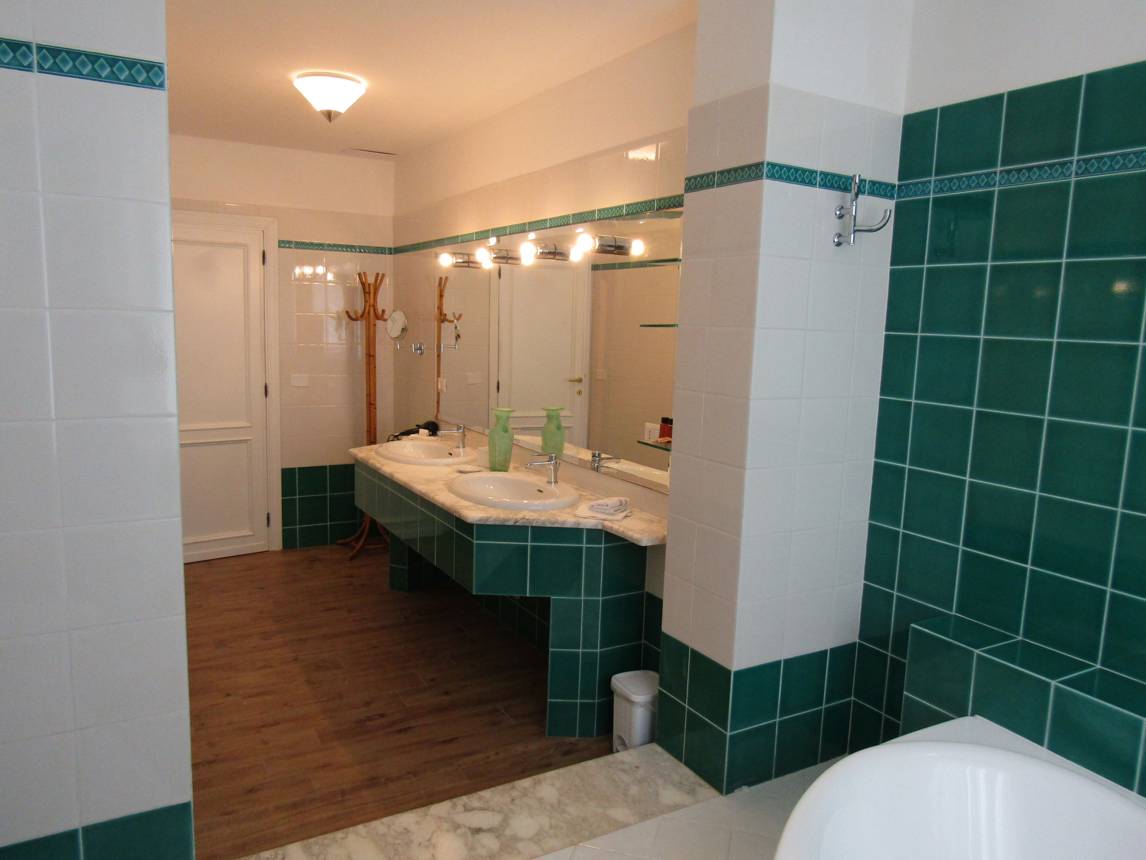 Un bagno con due lavandini, uno specchio e pareti piastrellate in verde.