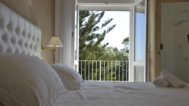A bedroom with a large bed, a wall-mounted lamp, and a balcony with a railing.