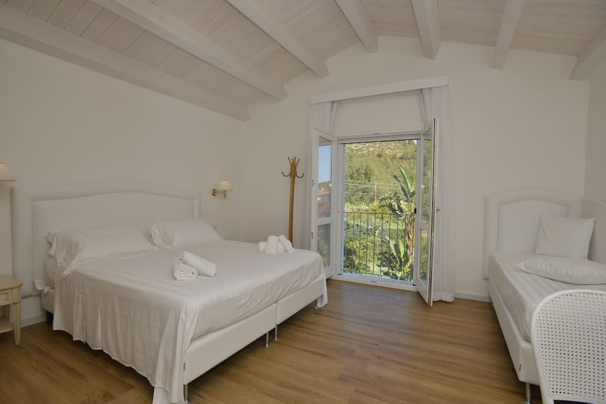 A bedroom with a bed, a chair, a nightstand, and a window with a view of greenery.