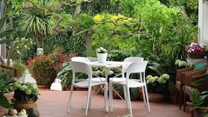 A patio area with a table and chairs, surrounded by various potted plants and flowers.